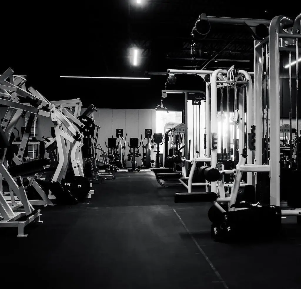 Un piso de entrenamiento vacío en Rhein Athletic Club, filas de máquinas de musculación bajo luz dramática contra un techo oscuro.