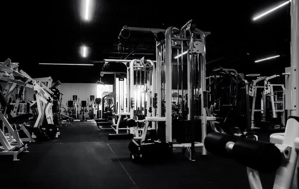 An empty training floor at Rhein Athletic Club, rows of weight machines under dramatic overhead lighting against a dark ceiling.
